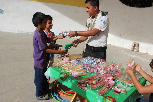 Un agente de la PNC de Puerto Barrios, Izabal entrega un carro de juguete a cambio de una pistola de agua. (Foto Prensa Libre: Edwin Perdomo)<br _mce_bogus="1"/>