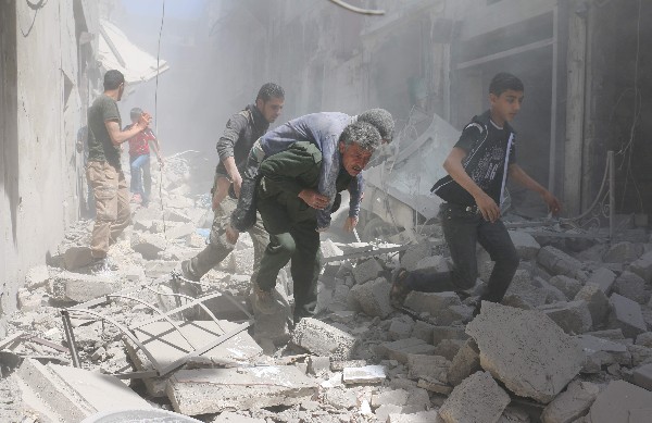 Sirios eyudan a un herido en medio de los escombros de un edificio en Alepo. (AFP).