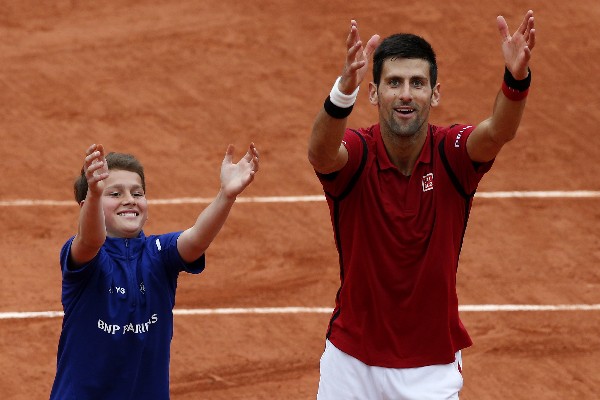Novak Djokovic celebra con un pequeño alcanza pelotas tras superar a Roberto Bautista, de España. (Foto Prensa Libre: EFE).