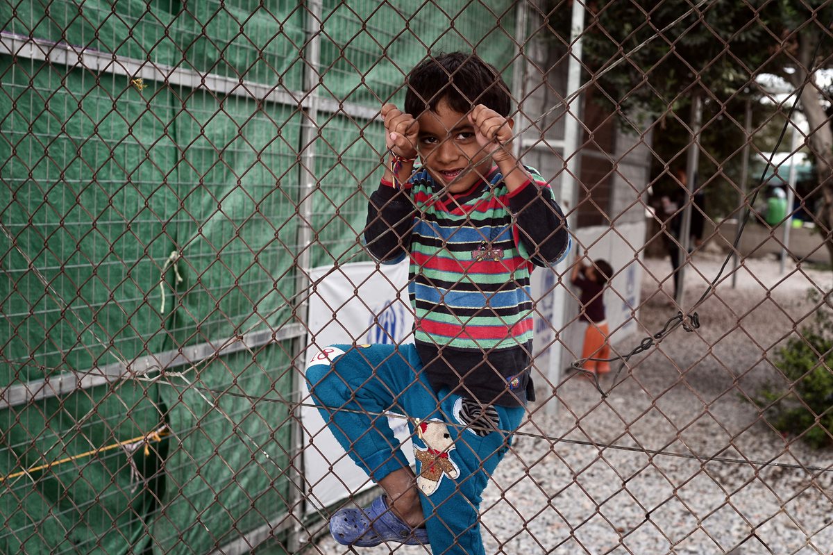 Un niño juega en la malla de un centro refugiados en Grecia. (Foto Prensa Libre: AFP).