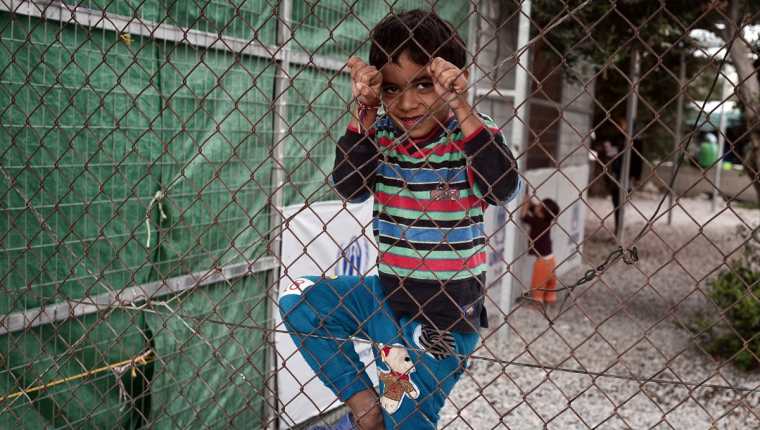 Un niño juega en la malla de un centro refugiados en Grecia. (Foto Prensa Libre: AFP).