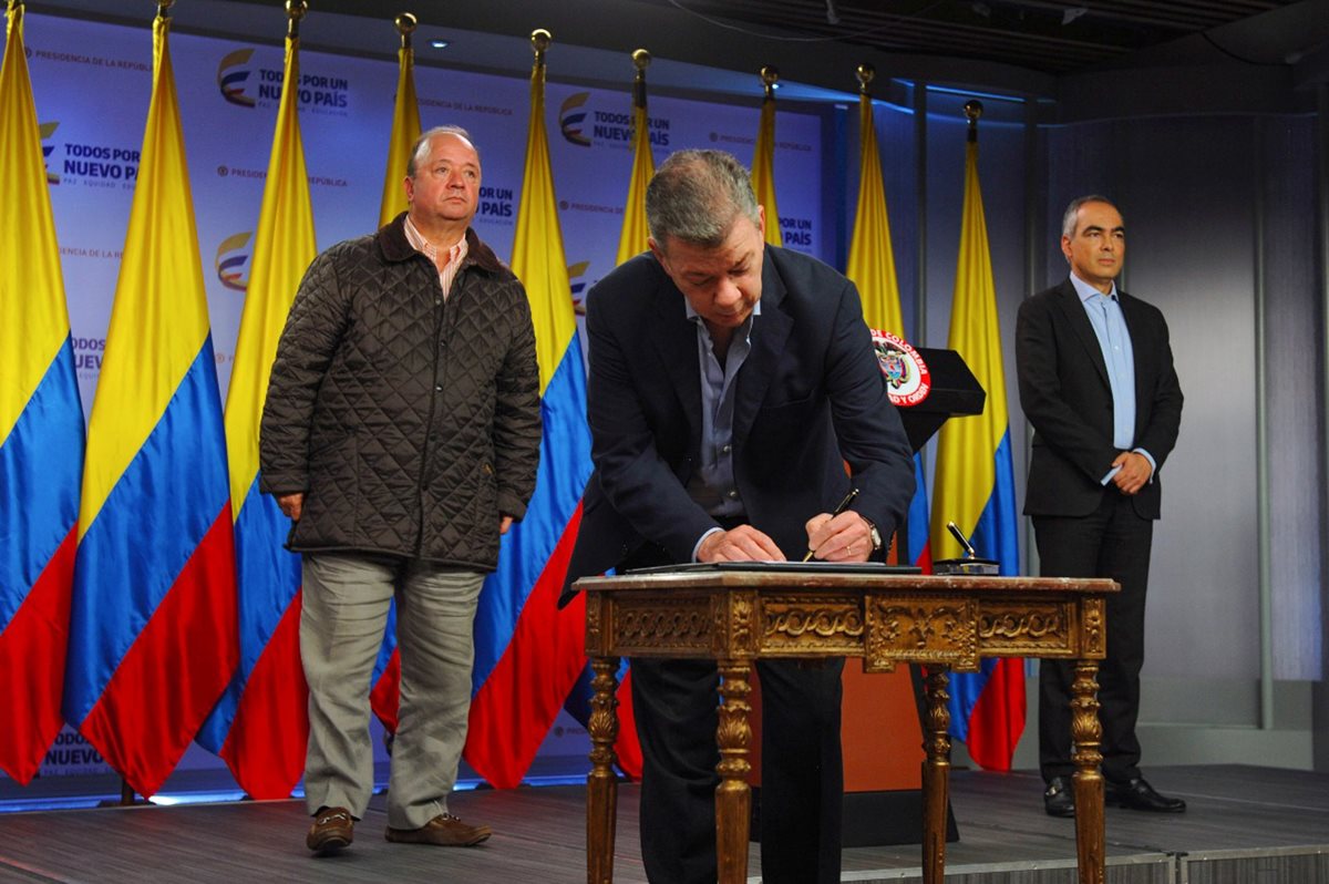 El presidente colombiano Juan Manuel Santos (C), acompañado por el ministro de Defensa Luis Carlos Villegas (i) y el comisionado por la Paz Rodrigo Rivera, firmando el alto el fuego con la guerrilla del ELN. (Foto Prensa Libre:AFP).