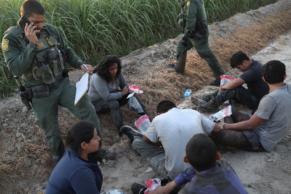 Agentes de la Patrulla Fronteriza vigilan a un grupo de inmigrantes detenidos en un campo de caña cerca de la frontera de EE. UU.-México. (AFP).