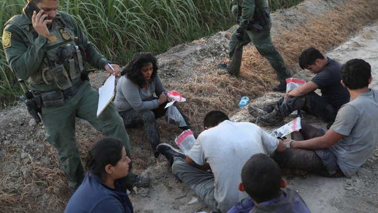 Agentes de la Patrulla Fronteriza vigilan a un grupo de inmigrantes detenidos en un campo de caña cerca de la frontera de EE. UU.-México. (AFP).