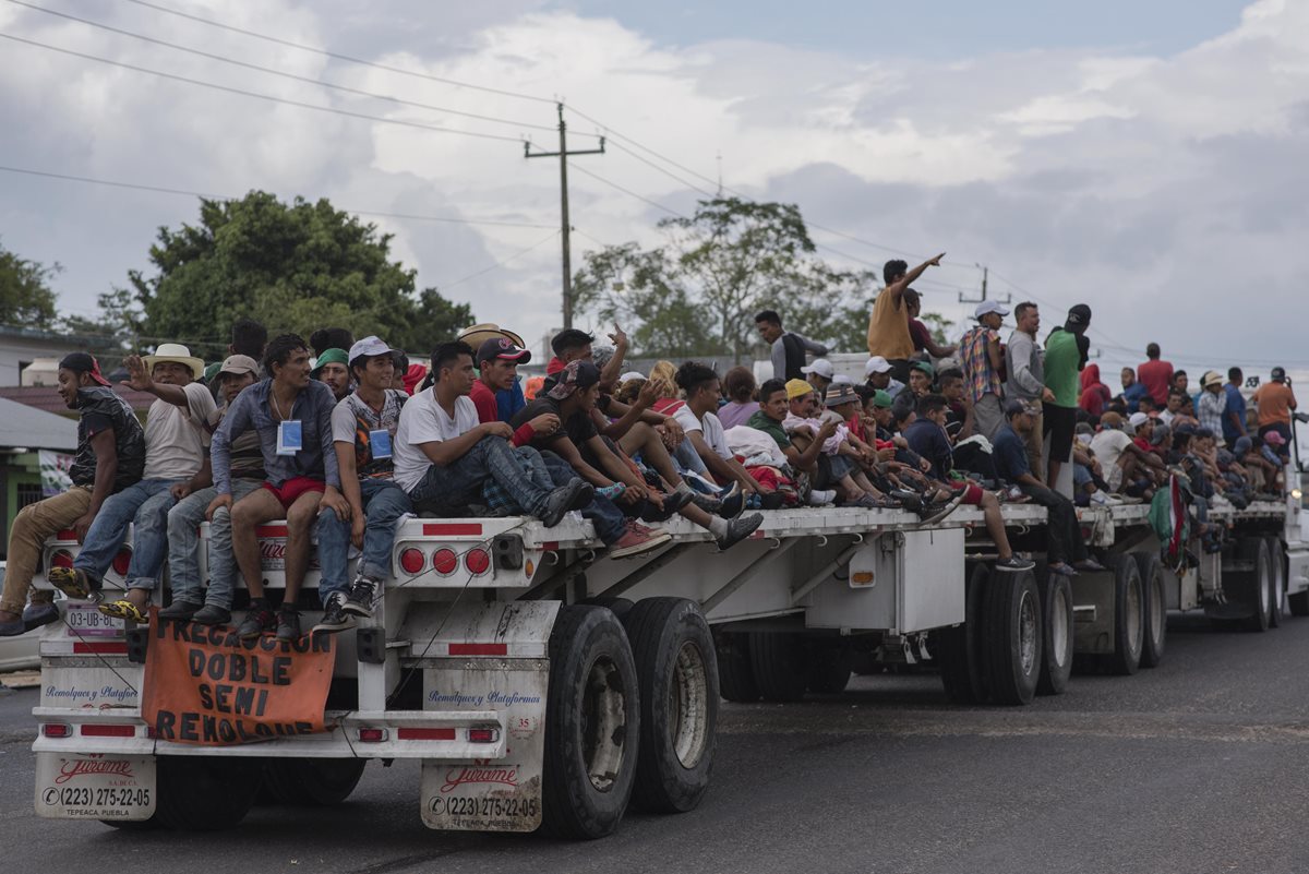 Migrantes aprovechan una plataforma jalada por un tráiler en Veracruz por el municipio de Sayula de Alemán. (Foto Prensa Libre: EFE)