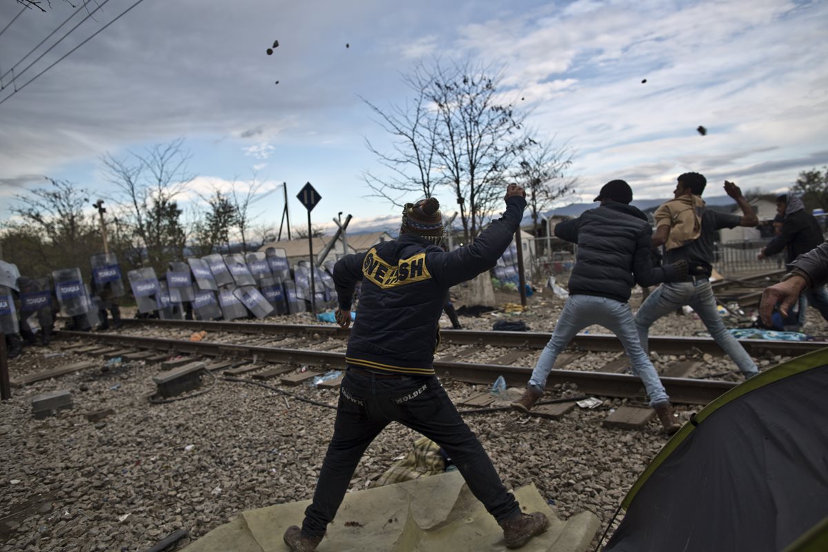 Migrantes atacan a pedradas a la policía macedonia. (Foto Prensa Libre: AP)