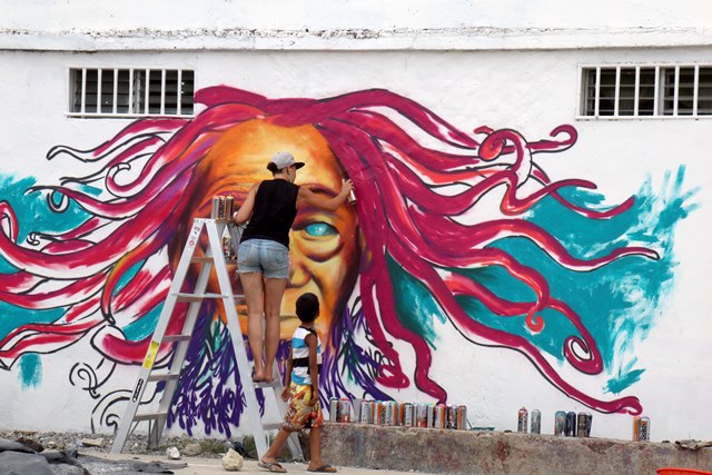 Un niño observa a la artista canadiense María Rosa Szychowska mientras pinta un mural en el barrio El Rastro, Puerto Barrios, Izabal. (Foto Prensa Libre: Dony Stewart)