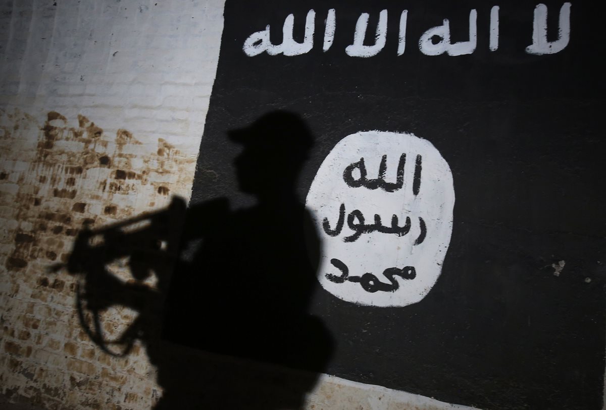 Un miembro de las fuerzas gubernamentales camina frente a una bandera que identifica al grupo terrorista Estado Islámico. (Foto Prensa Libre: AFP)