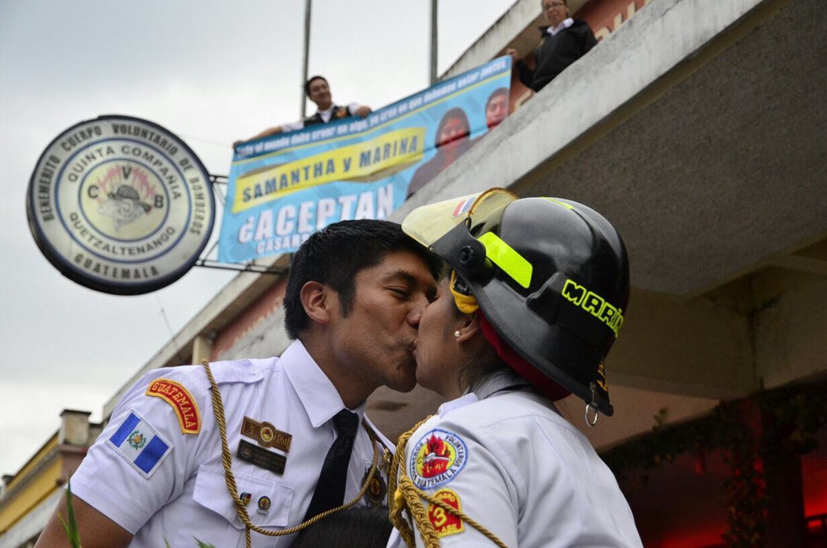 Los compañeros de Carlos le ayudaron sosteniendo, en la Estación de Bomberos Voluntarios, un cartel pidiéndole matrimonio a Marina, ambos son socorristas. (Foto, Prensa Libre: Stereo 100)