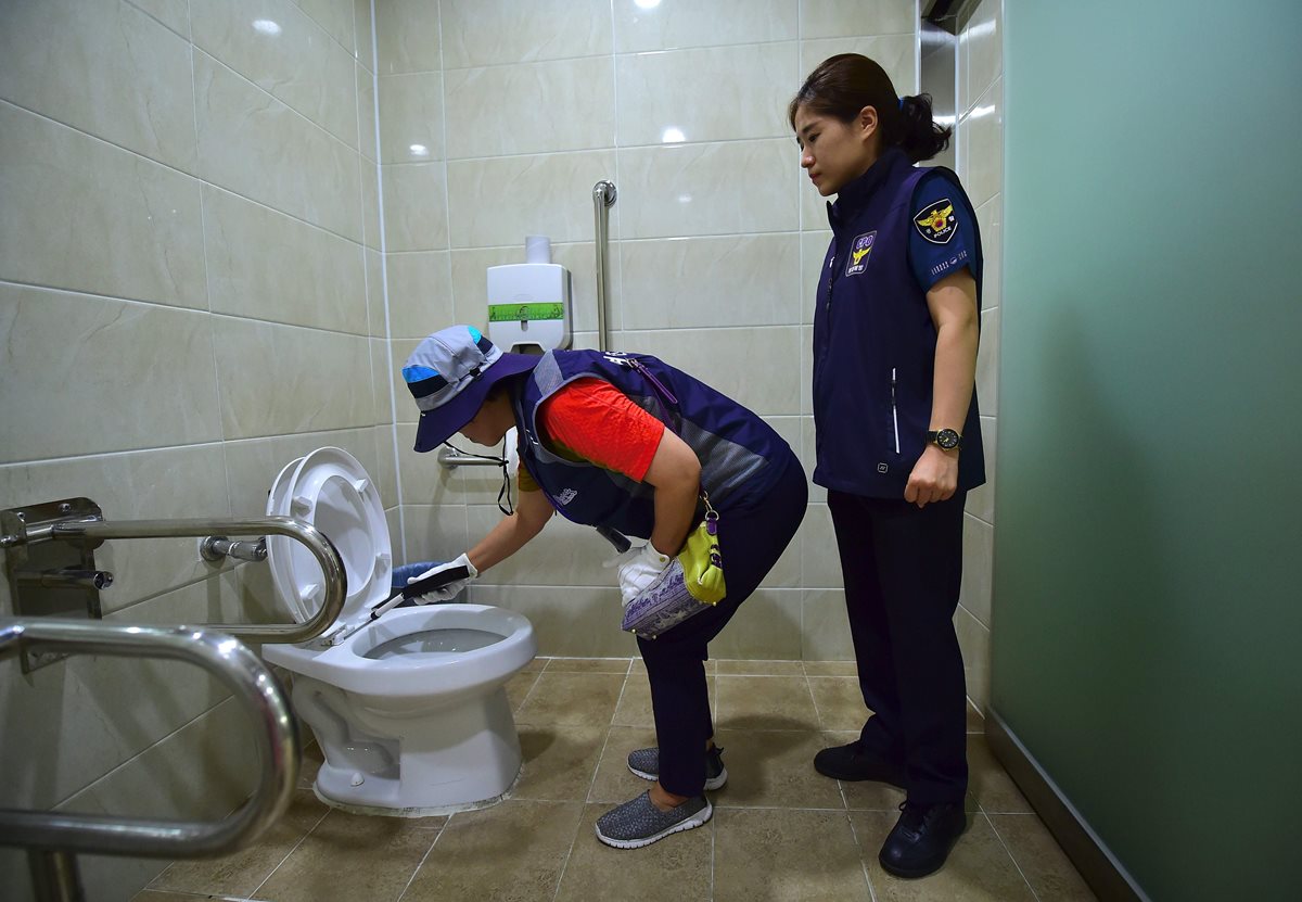 Dos empleadas revisan detalladamente un sanitario de mujeres en Seúl, en busca de "cámaras ocultas" que buscan grabar a las féminas. (Foto Prensa Libre: AFP).