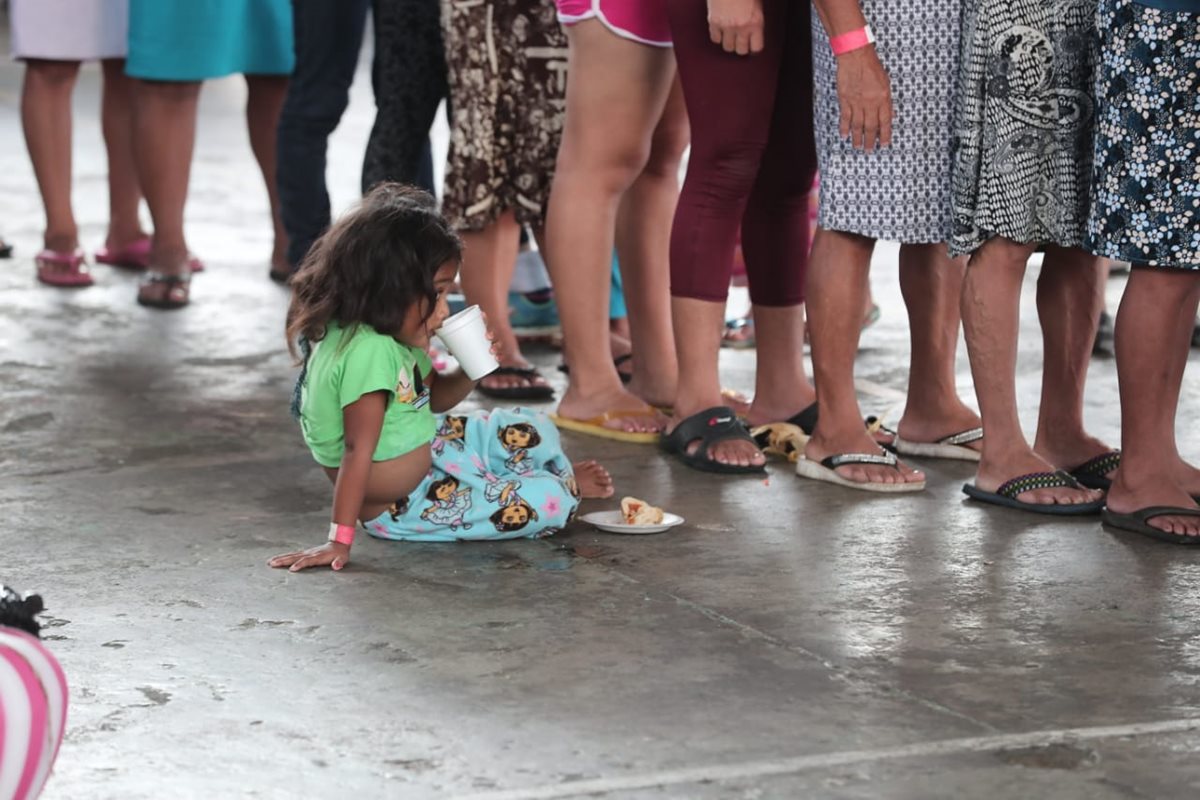 Una niña espera a su mamá mientras hacen fila para recibir ayuda.