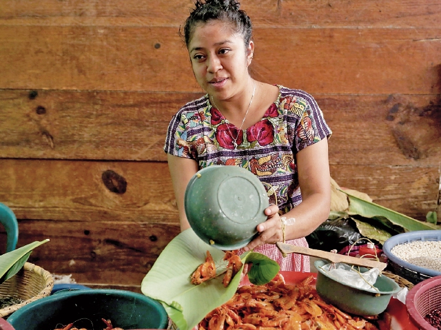 María atiende su venta de mariscos en el mercado de San Pedro La Laguna y dejó de utilizar bolsas de plástico, ahora entrega su producto  en hojas de plátano. (Foto Prensa Libre: EFE)