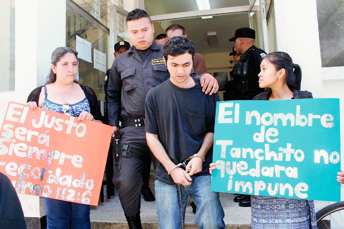 Dos mujeres sostienen dos carteles que recuerdan a la víctima. Sale del juzgado Jonathan Widmar Berreondo, uno de los dos acusados, en Santa Cruz del Quiché. (Foto Prensa Libre: Óscar Figueroa)