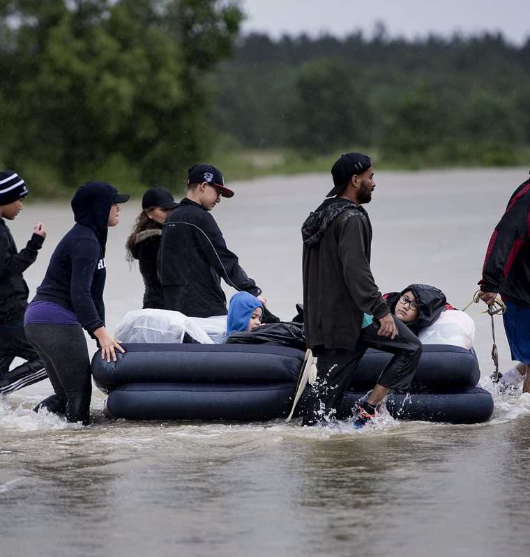 Varios pobladores escapan de un vecindario inundado usando un colchón inflable en Houston, Texas.(AFP).