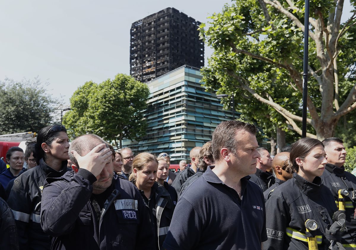 Socorristas participan en el minuto de silencio frente al Grenfell Tower en Londres, donde decenas de personas murieron a causa de un incendio. (Foto Prensa Libre: AP)