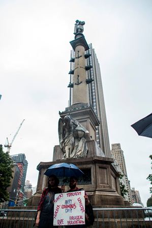 Dos manifestantes exhiben un cartel donde pididen la eliminación de la estatua de Cristóbal Colón en Nueva York. (AFP).