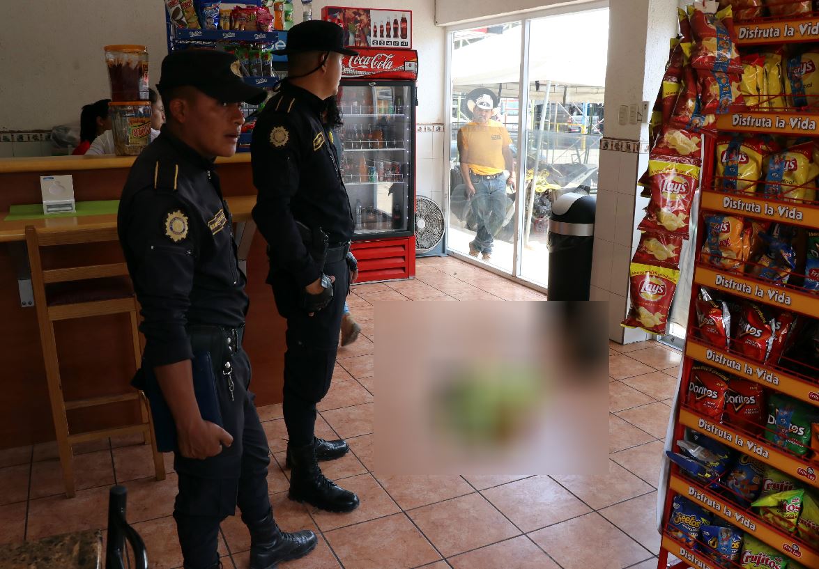 Policías observan el cadáver del menor, dentro de la tienda de Jalapa, al fondo, un curioso. (Foto Prensa Libre: Hugo Oliva)