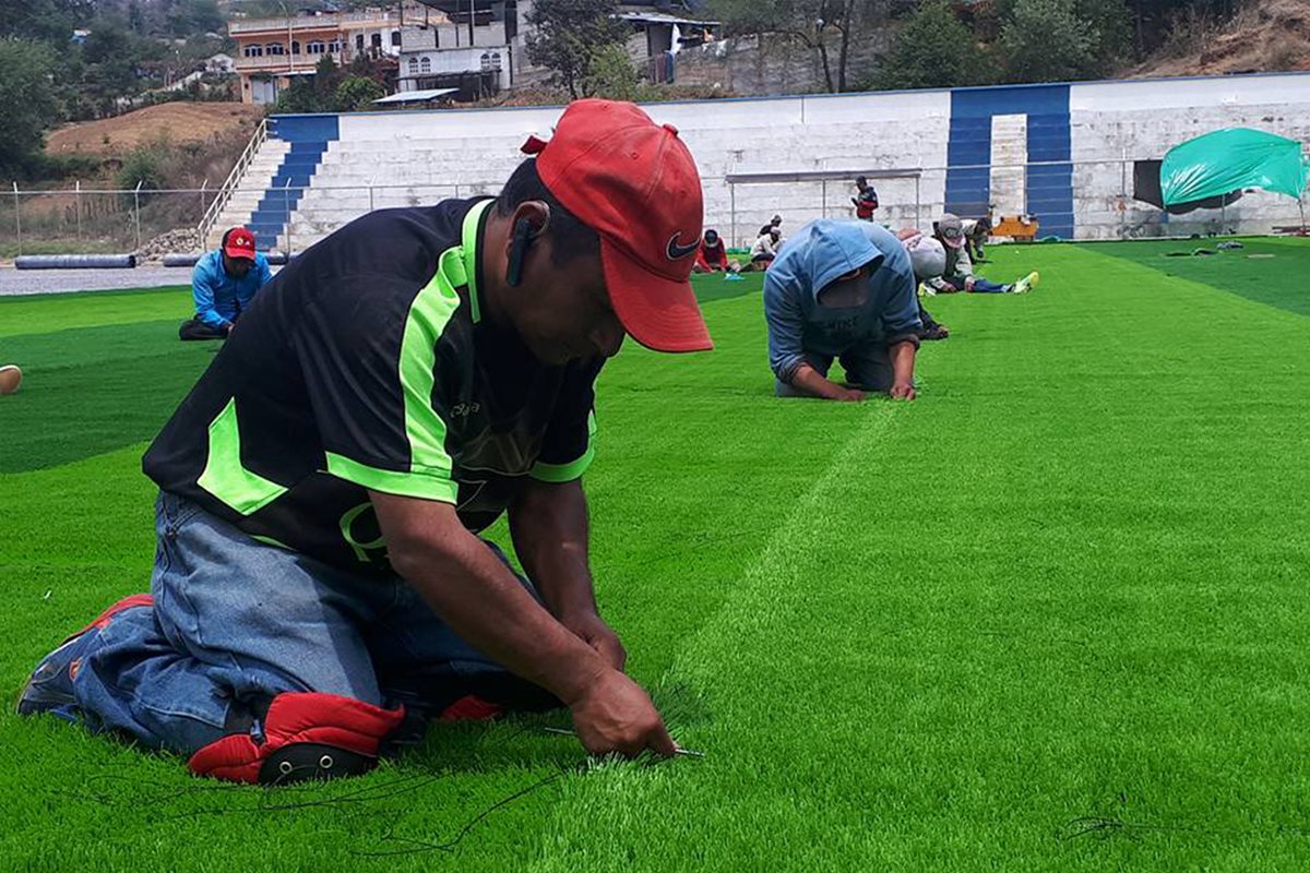 Empleados de la empresa contratada instala la gramilla sintética en el campo de futbol de Comitancillo. (Foto Prensa Libre: Whitmer Barrera)