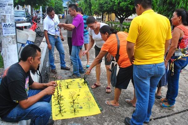 Mayco Escobar elabora una figura, mientras Óscar, de playera violeta, muestra los productos. (Foto Prensa Libre: Jorge Tizol)