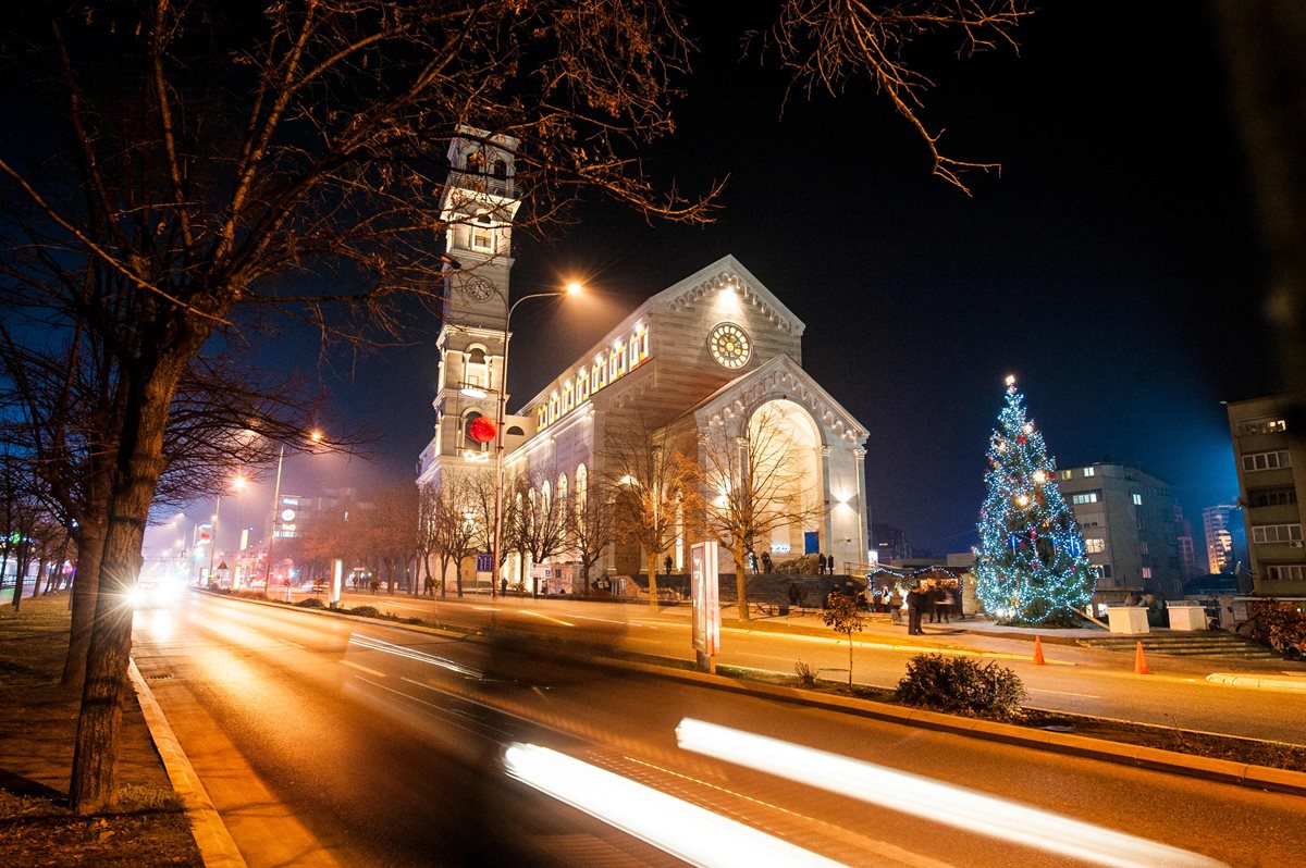 Varios automóviles pasan frente a la catedral de la Madre Teresa antes de la Misa de Gallo en Pristina. (AFP).
