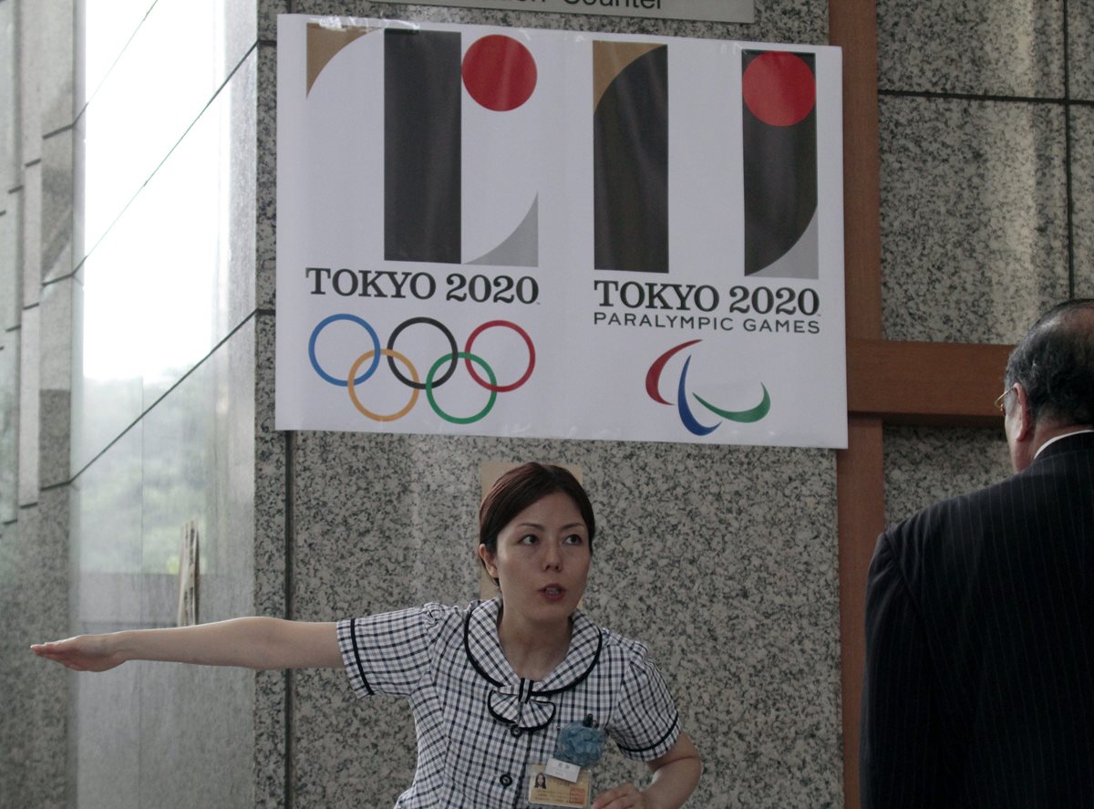 Una recepcionista da indicaciones a un visitante bajo el logo de los Juegos Olímpicos de Tokio 2020 en Tokio. (Foto Prensa Libre: EFE)