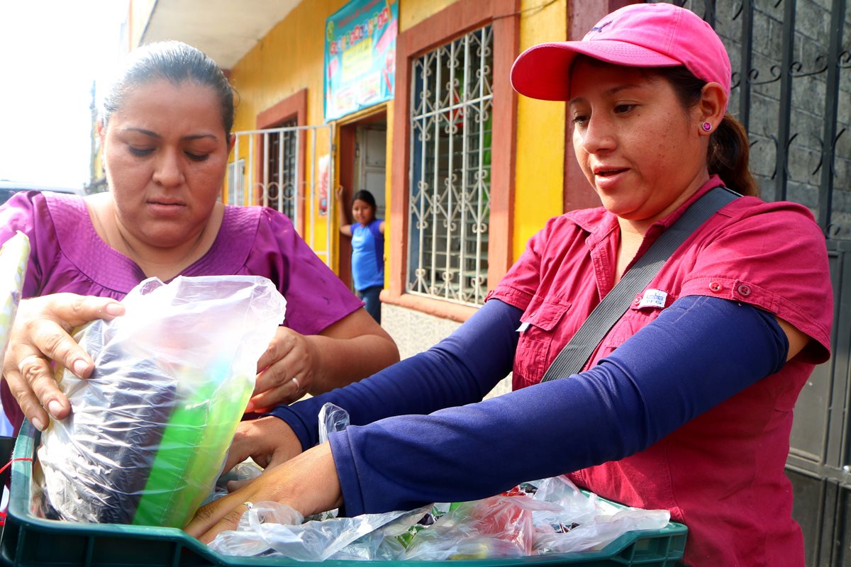 Jaqueline Zepeda (con gorra) acomoda las bolsas de "cuquitos" en una canasta plástica para salir a vender en motocicleta. (Foto Prensa Libre: Rolando Miranda)