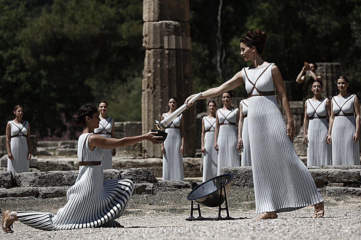La actriz griega Katerina Lehú (de pie), en el papel de la Gran Sacerdotisa de Olimpia, enciende la llama durante la ceremonia de encendido de la antorcha olímpica en el templo de Hera, en la antigua Olimpia, Grecia. (Foto Prensa Libre: EFE)