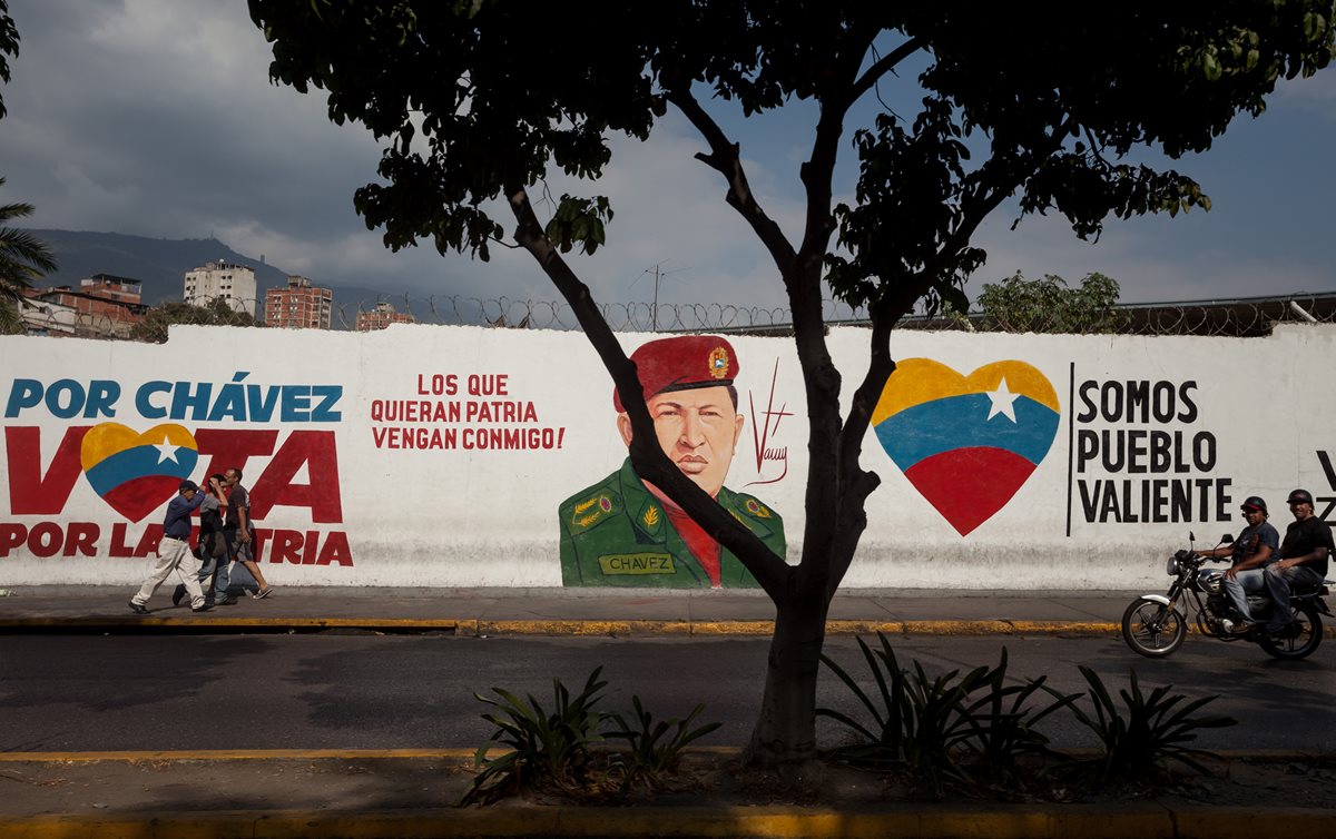 Varias personas pasan frente a un mural en honor del fallecido presidente venezolano Hugo Chávez en Caracas, Venezuela. (Foto Prensa Libre: EFE).