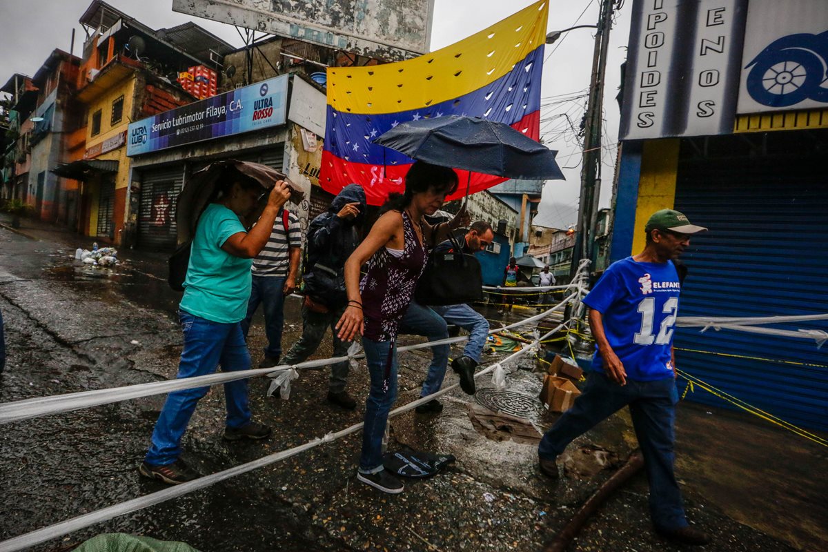 Transeúntes cruzan una calle bloqueada por manifestantes opositores en Caracas.(Foto Prensa Libre: EFE).