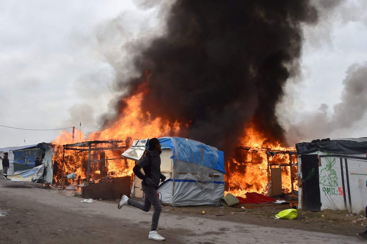 Un refugiado corre frente a las precarias viviendas en llamas en el campamento de migrantes de Calais. (Foto Prensa Libre: AFP).