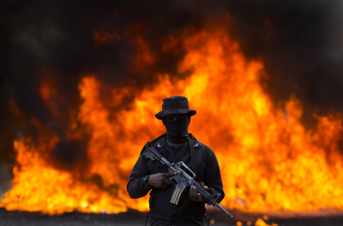 Cientos de kilos de diferentes drogas son incinerados en República Dominicana, mientras un soldado resguarda el área. (Foto Prensa Libre: EFE)