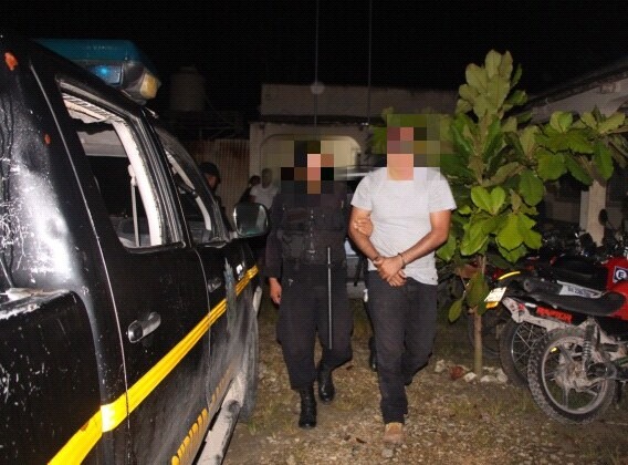 Agente de la PNC custodia a uno de los capturados en Dolores, Petén. (Foto Prensa Libre: PNC).