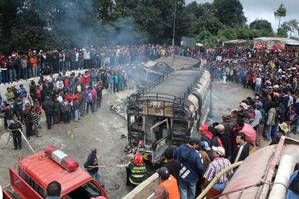 Centenares de curiosos observan los restos del camión y del autobús, luego de que los bomberos sofocaran las llamas.