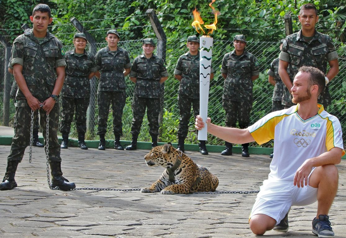 Un atleta sostiene una antorcha mientras el jaguar "Juma" es exhibido durante el acto. (Foto Prensa Libre: AFP).
