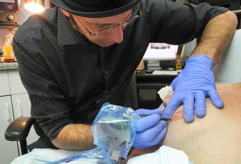 En su tienda, Vincent  Vinnie Myers realiza un tatuaje a una mujer sobreviviente de cáncer de mama. (Foto Prensa Libre: AFP)