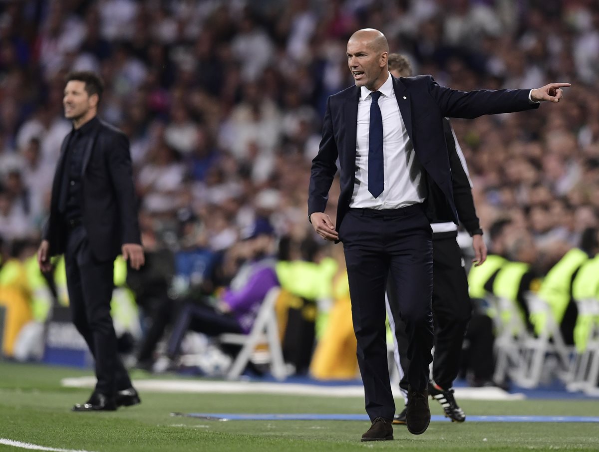 Los técnicos Zinedine Zidane del Real Madrid y Diego Simeone (al fondo) dan instrucciones desde su área técnica.