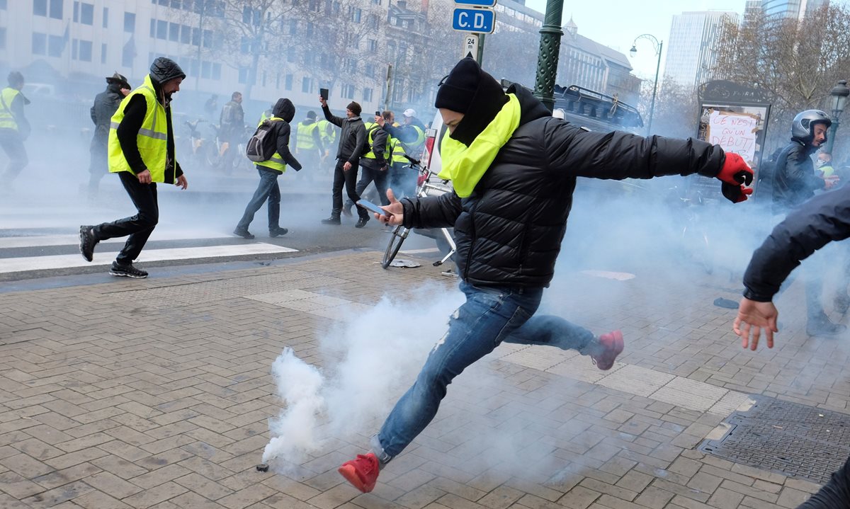 Un manifestante del colectivo "chalecos amarillos" trata de devolver un cartucho de gas lacrimógeno durante una protesta contra la subida de los impuestos a los carburantes. (Foto Prensa Libre: EFE)