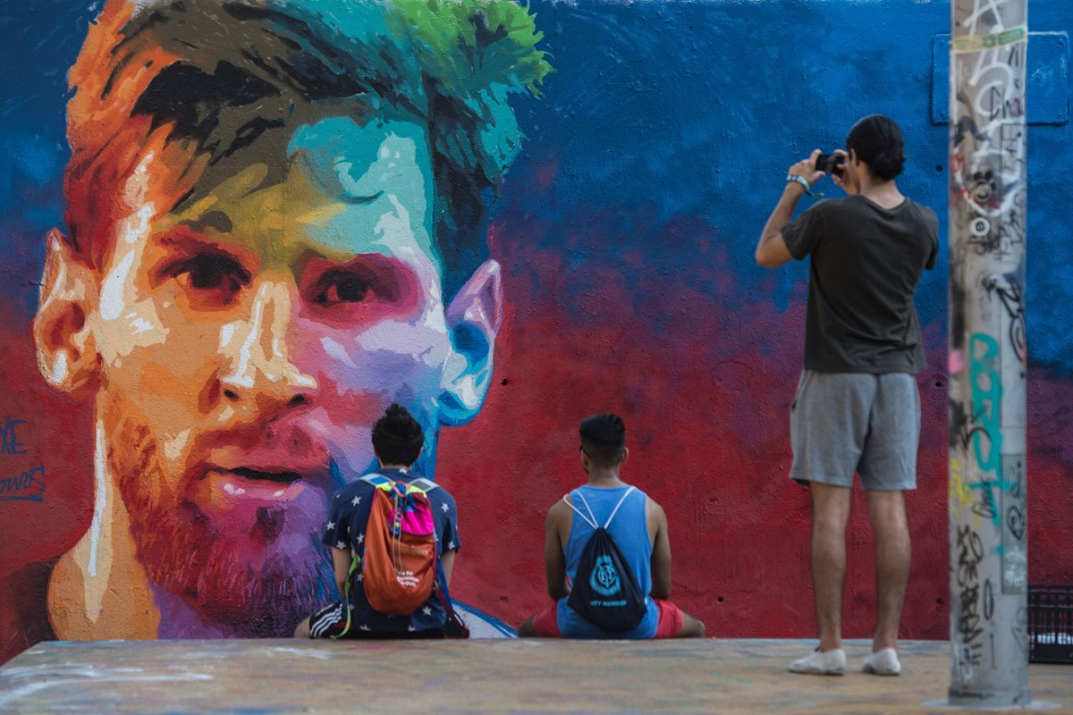 El presidente del Real Madrid, Florentino Pérez, aseguró que le hubiera gustado tener en su equipo a Leo Messi. En la foto dos jovenes observan un mural con el rostro de Messi. (Foto Prensa Libre: AFP)