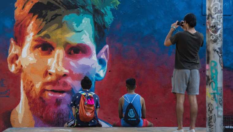 El presidente del Real Madrid, Florentino Pérez aseguró que le hubiera gustado tener en su equipo a Leo Messi. Dos jovenes observan un mural con el rostro de Messi. (Foto Prensa Libre: AFP)