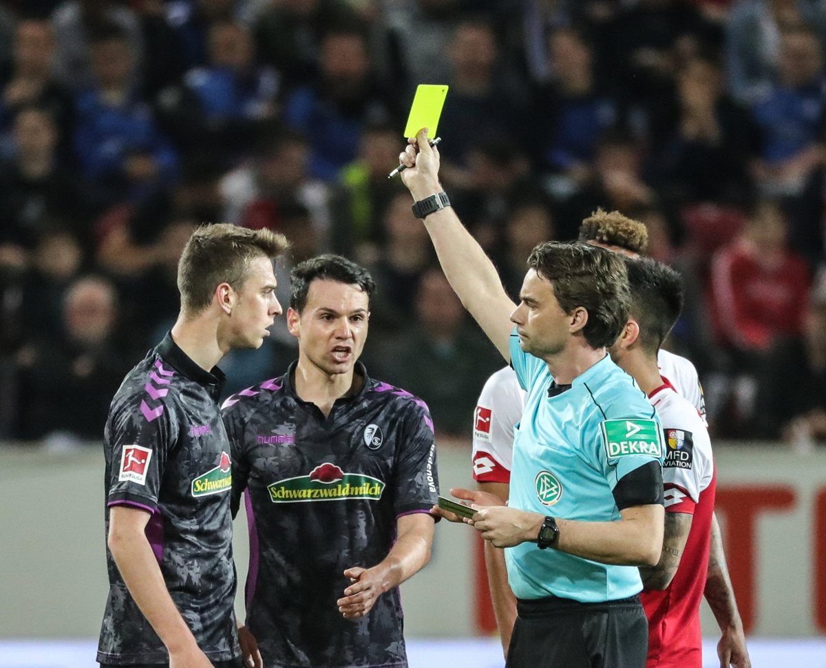 El árbitro Guido Winkmann (d) muestra la tarjeta amarilla a Janik Haberer (i) de Friburgo. (Foto Prensa Libre: AFP)