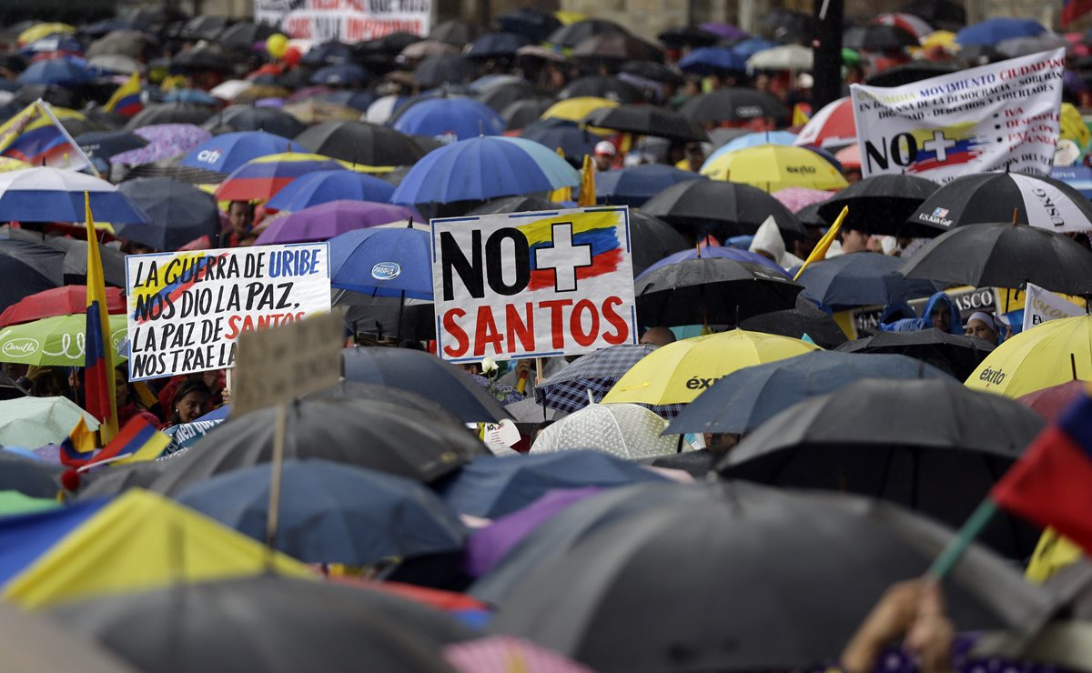 Manifestantes rechazan al gobierno de Juan Manuel Santos mientras se cubren de la lluvia que cayó en Bogotá. (Foto Prensa Libre: AP).