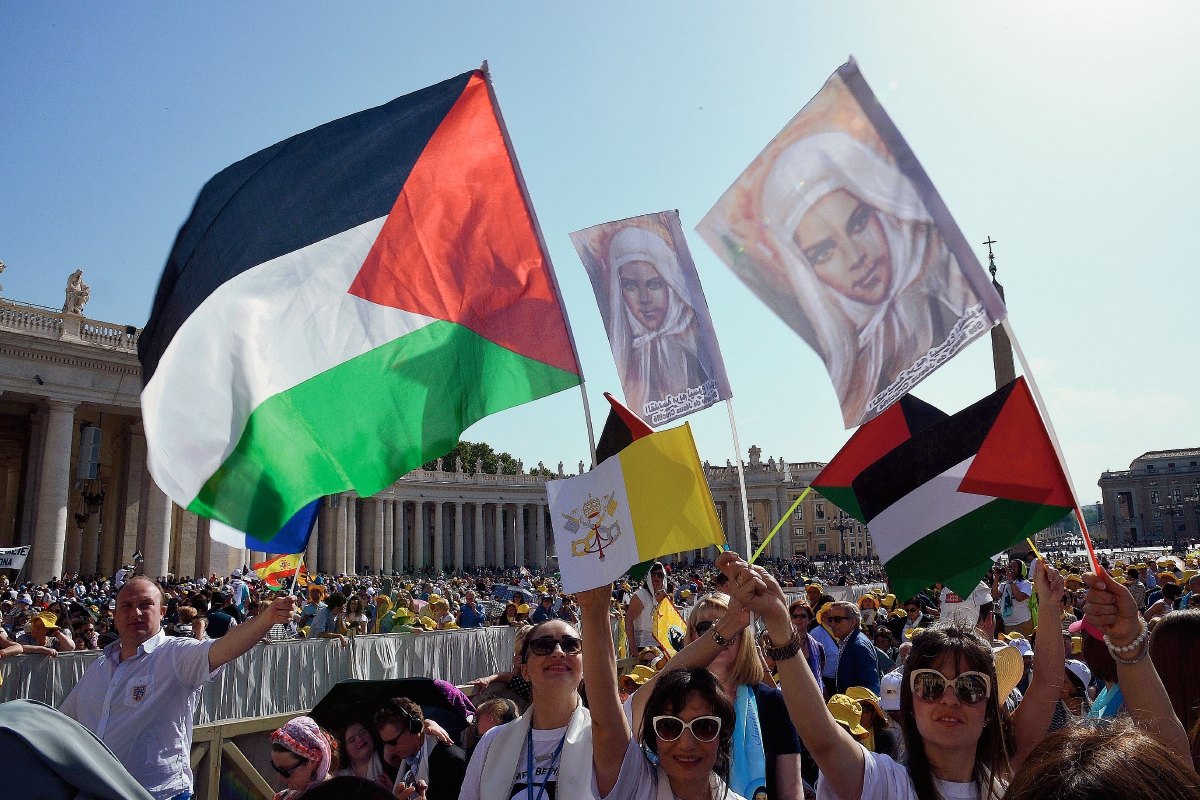 Peregrinos ondean  banderas palestinas antes de una misa en la plaza de San Pedro para la canonización de cuatro monjas. (Foto Prensa Libre:AFP).
