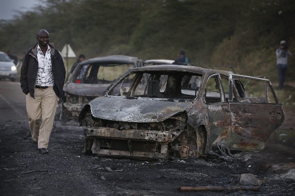 Un hombre camina junto a los automóviles quemados en la carretera cerca de Naivasha. (Foto Prensa Libre: EFE)