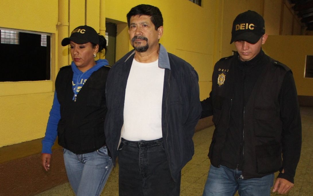 Uno de los capturados, sindicado de peculado y uso de documentos falsificados, es trasladado por la PNC. (Foto Prensa Libre: PNC)