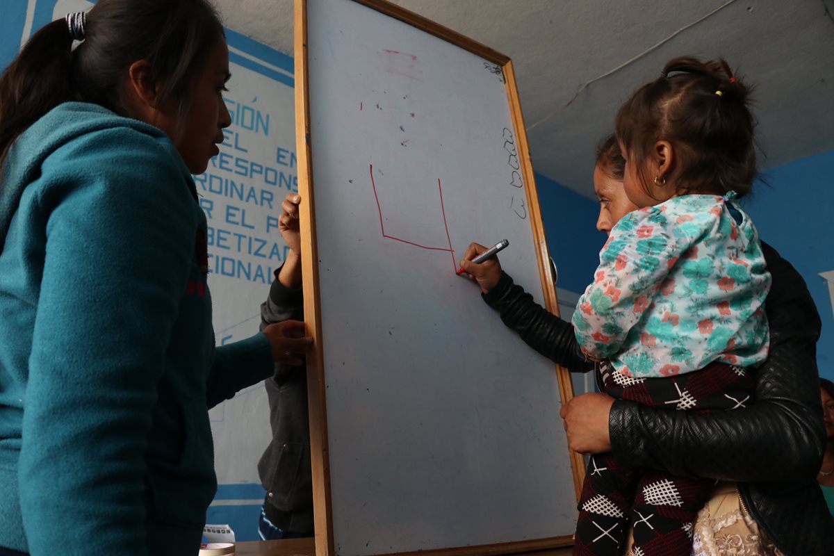 Una mujer con su hija en brazos escribe en una pizarra en Huehuetenango. (Foto Prensa Libre: Mike Castillo)