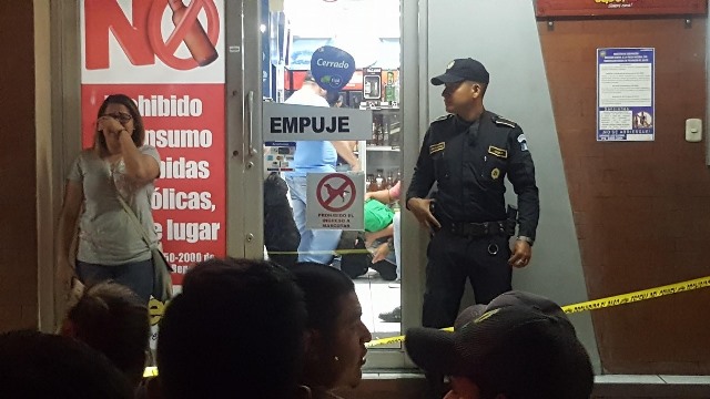 Un agente policial vigila la escena del crimen, mientras que otras personas se muestran muy afectadas por lo ocurrido en el interior del negocio. (Foto Prensa Libre: Mario Morales)