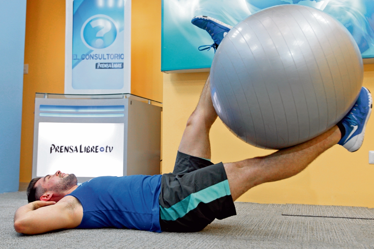 Abdominales inferiores. Acostarse en el suelo y extender las piernas de forma horizontal con la pelota en medio de ellas. Levantar lentamente y mantener los hombros relajados. Repetir por un minuto. (Foto Prensa Libre: Óscar Rivas).