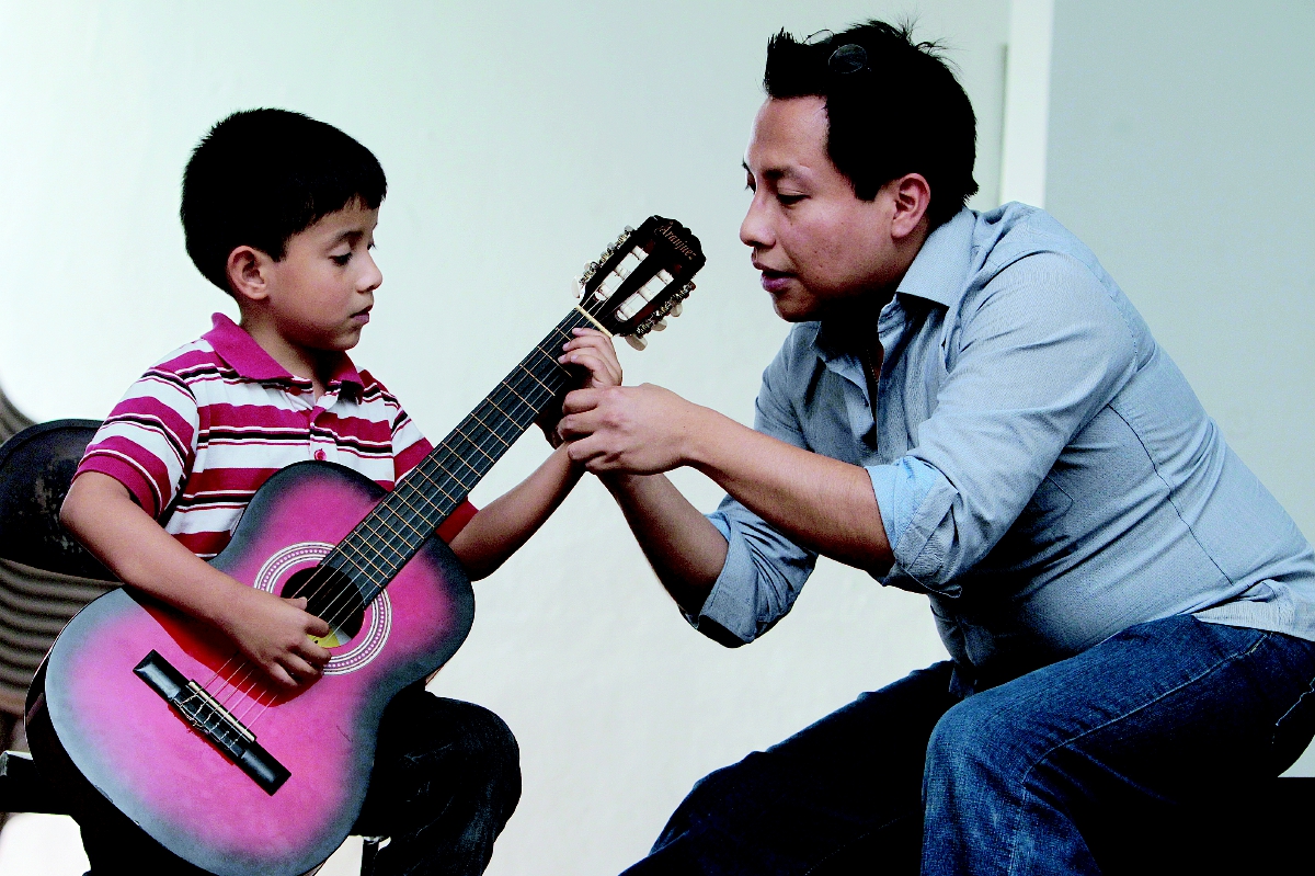 Dilan Gómez, de 7 años, atiende los consejos de Luis Juárez Quixtán, para tocar correctamente la guitarra. (Foto Prensa Libre: Edwin Castro).