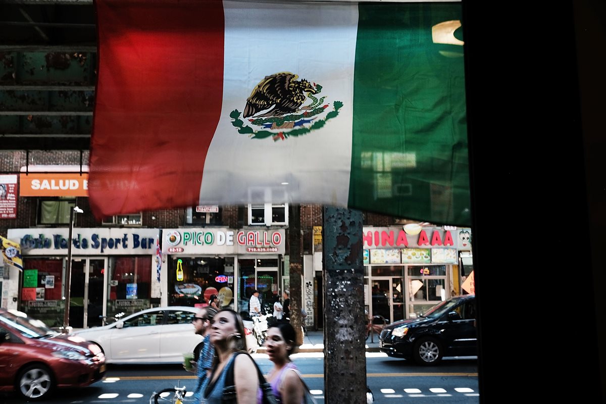 Personas caminan bajo una bandera mexicana en el famoso y multiétnico barrio Queens de Nueva York. (Foto Prensa Libre: AFP).