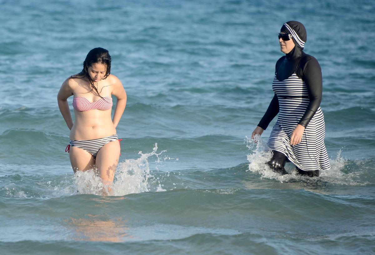 Una mujer musulmana luce un burkini (traje de baño islámico), en contraste con otra que luce un traje de baño convencional. (Foto Prensa Libre: AFP).